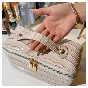 Close-up of a beige croc-pattern makeup bag with a sturdy handle and gold zippers.