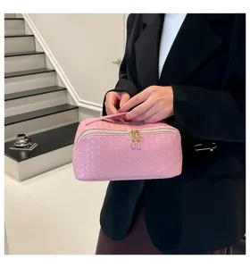 Grote roze geweven cosmetische tas met gouden ritsen vastgehouden door een persoon