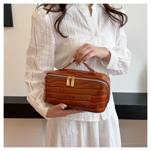 Close-up detail of a brown crocodile embossed cosmetic bag with gold-tone double zippers