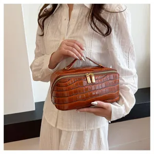 Detailed view of brown croc-embossed travel cosmetic bag with double gold zippers