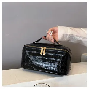Detailed view of black crocodile pattern cosmetic bag with gold zippers and handle