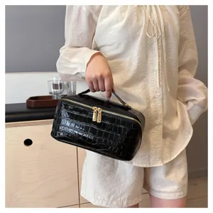Model holding a black glossy crocodile pattern makeup bag with gold hardware detail.