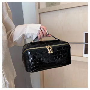 Detailed view of the glossy black croc-embossed vanity bag with gold zippers.
