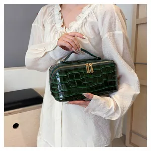 Detailed view of emerald green crocodile embossed cosmetic bag with gold zippers