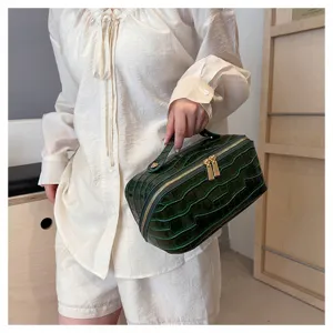 Detail shot of a dark green crocodile pattern large capacity makeup bag held by hand