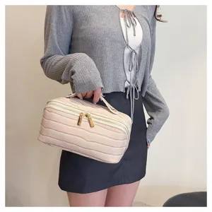 Detail of cream crocodile pattern cosmetic bag held by a person in a grey cardigan