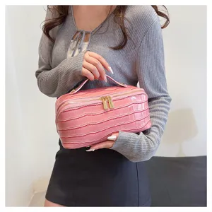 Detailed view of a pink crocodile-embossed cosmetic bag being held by a female model