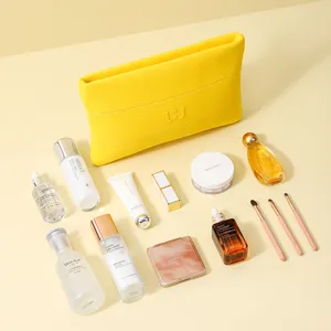 Große gelbe Kosmetiktasche aus Neopren mit verschiedenen Make-up-Artikeln umgeben.