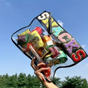 Close-up of a clear PVC snack pouch with colorful embroidered letters held outdoors.