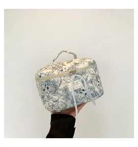 Close-up of a blue floral quilted cotton makeup bag with handle and zipper closure
