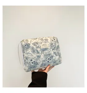Close-up view of a quilted cotton makeup bag featuring blue floral print and ribbon zipper