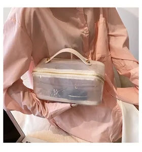 Large transparent travel makeup bag with white handle held by model in pink shirt