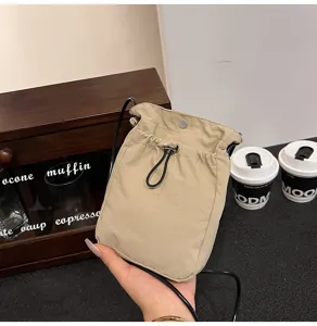 Primer plano de un mini bolso bandolera de lona beige con cordón sostenido en la mano.