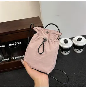 Detalle de un mini bolso rosa minimalista de lona con cordón para el móvil sostenido en la mano