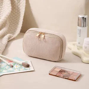 Nahaufnahme einer beigen Cord-Kosmetiktasche mit goldenen Reißverschlüssen.