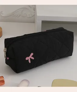 Gros plan d'une trousse à maquillage en coton matelassé noir avec un nœud rose brodé.