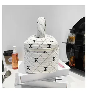 Stylish corduroy bucket makeup bag with black bow print on a white desktop setup.