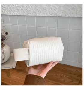 Hand-held detail of a white quilted PU leather makeup bag with a sturdy side handle.
