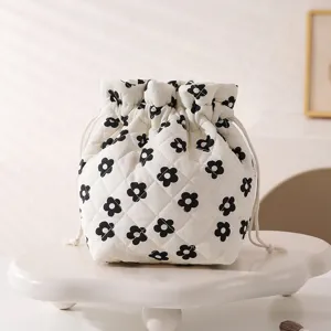 Close-up of white quilted drawstring cosmetic pouch featuring a black floral pattern