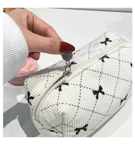 Detail view of a white corduroy makeup bag with black bow prints and a smooth zipper.