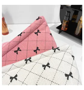 Close-up of corduroy cosmetic bags with bow print and quilted pattern in pink and white.