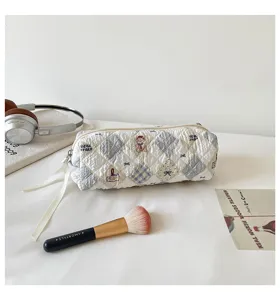 Detail of a soft quilted makeup bag with cute bear embroidery and blue plaid pattern.