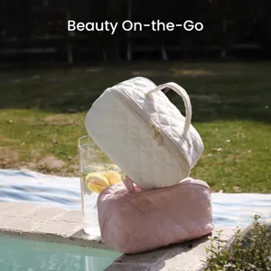 Close-up of portable quilted travel makeup bags in white and pink by a sunlit swimming pool