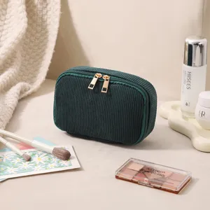 Dunkelgrüne Cord-Kosmetiktasche umgeben von Kosmetik auf beigem Hintergrund
