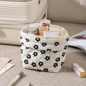 Detail view of cream quilted drawstring makeup bag with black floral print and cosmetics