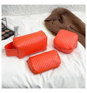 Three orange PU leather quilted cosmetic bags on a white textured surface with props.
