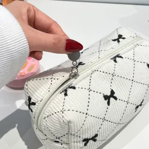 Detail view of the silver zipper and bow pattern on the white corduroy makeup bag