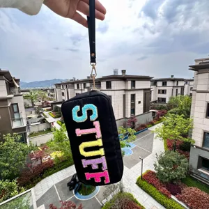 Détail d'une pochette en nylon noir avec broderie STUFF en chenille colorée tenue à la main