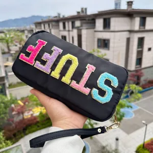 Gros plan d'une trousse à maquillage en nylon noir avec broderie STUFF colorée.