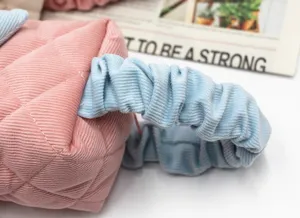 Detailed close-up of pink quilted corduroy cosmetic bag with a blue ruffled handle strap
