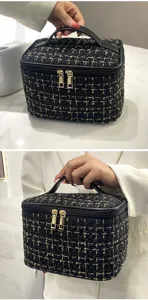 Detail view of a large black and gold tweed cosmetic bag with handle and dual zippers.