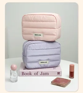 Two pastel puffer cosmetic bags stacked on a book with makeup accessories around