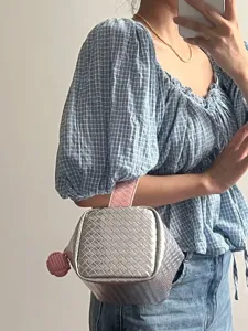 Nahaufnahme einer silber-rosa geflochtenen Kosmetiktasche, gehalten von einem Modell