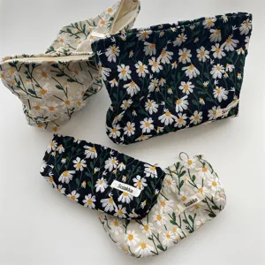 Close-up detail of embroidered daisy makeup pouches in black and beige canvas