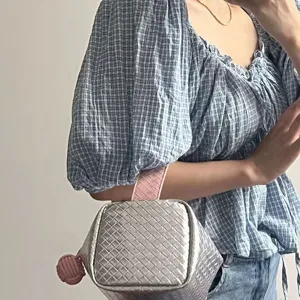 Detailansicht einer silbern-rosa geflochtenen Kosmetik-Handtasche, von Modell getragen