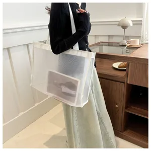 Bolso tote grande de malla transparente blanca llevado por una modelo en un café