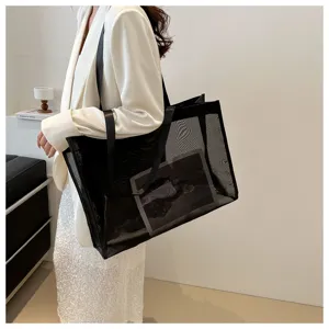 Elegante bolso tote de malla negra llevado por una modelo en un entorno minimalista