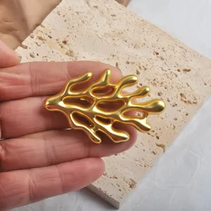Close-up detail view of a matte gold coral-shaped brooch held in hand against a textured stone slab