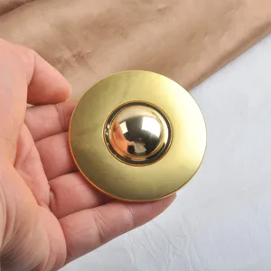 Close-up view of a large gold mirror finished round brooch held in a hand for scale