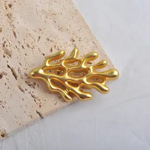 Close-up of matte gold coral brooch on stone texture, showing niche ocean design details.