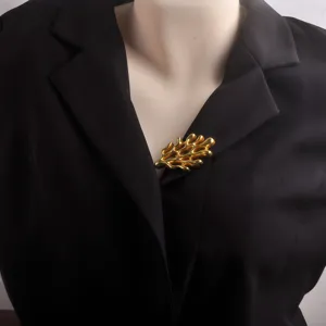 Detail view of a matte gold coral brooch pinned on a black suit blazer lapel.