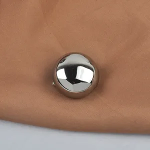 Close-up of a fashionable round metallic glossy brooch on brown fabric.