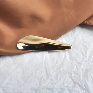 Vue détaillée d'une élégante broche dorée en métal abstrait au design ondulé