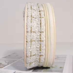 Détail latéral d'une mini trousse à maquillage en tweed blanc et doré avec fermeture.