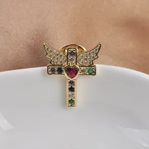 Close-up of elegant golden winged cross brooch with heart and colorful rhinestones