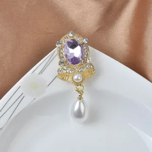 Nahaufnahme einer Magnetbrosche mit lila Edelstein, Kristallen und Perlenanhänger.